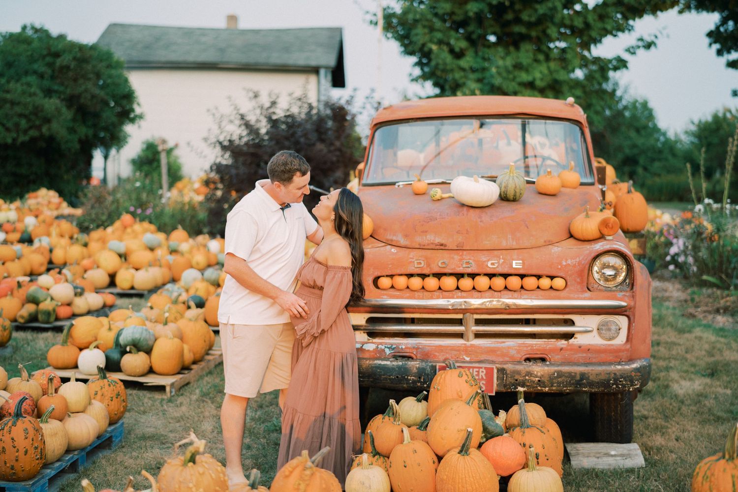 A couple shares a moment together amid a pumpkin patch beside a vintage orange truck.