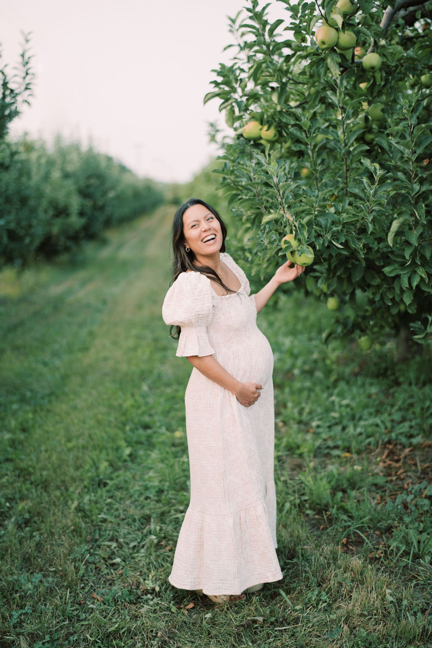 A joyful moment captured in a sunlit apple orchard wearing a flowing white dress.
