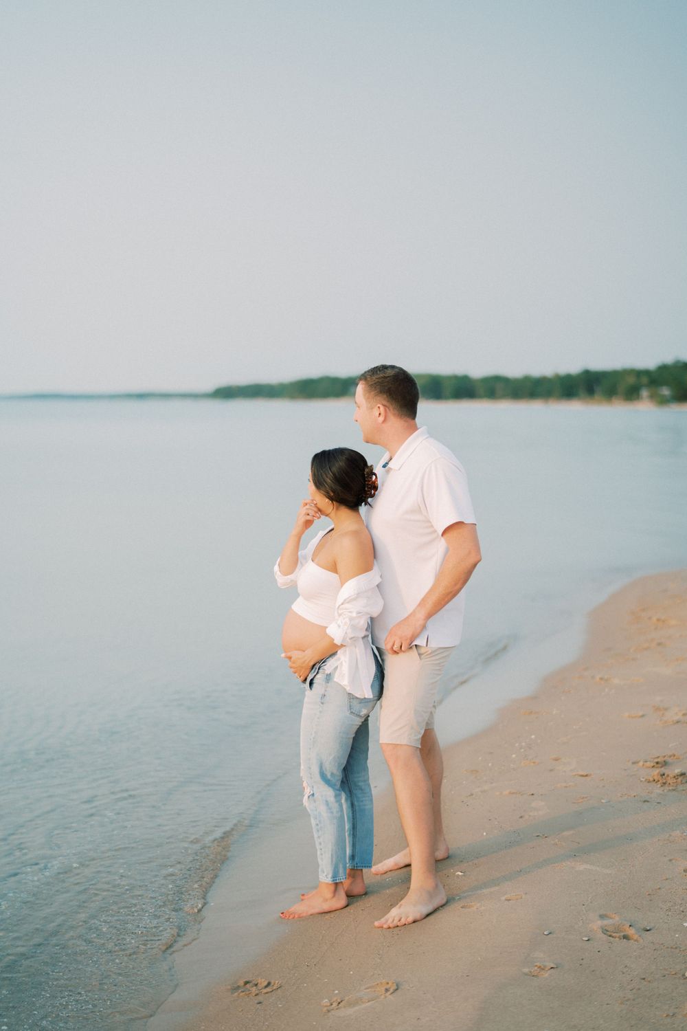 Couple shares intimate moment during beach maternity photoshoot at sunset.