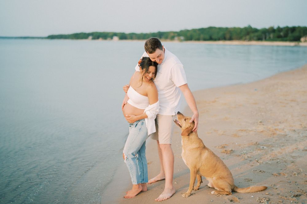 Maternity beach photo with couple and their golden retriever at sunset.