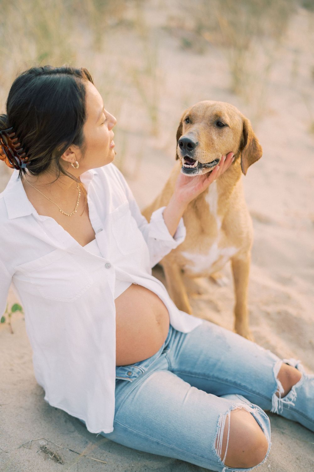 A joyful beach maternity photo captures a sweet moment between a golden retriever and expectant mother.
