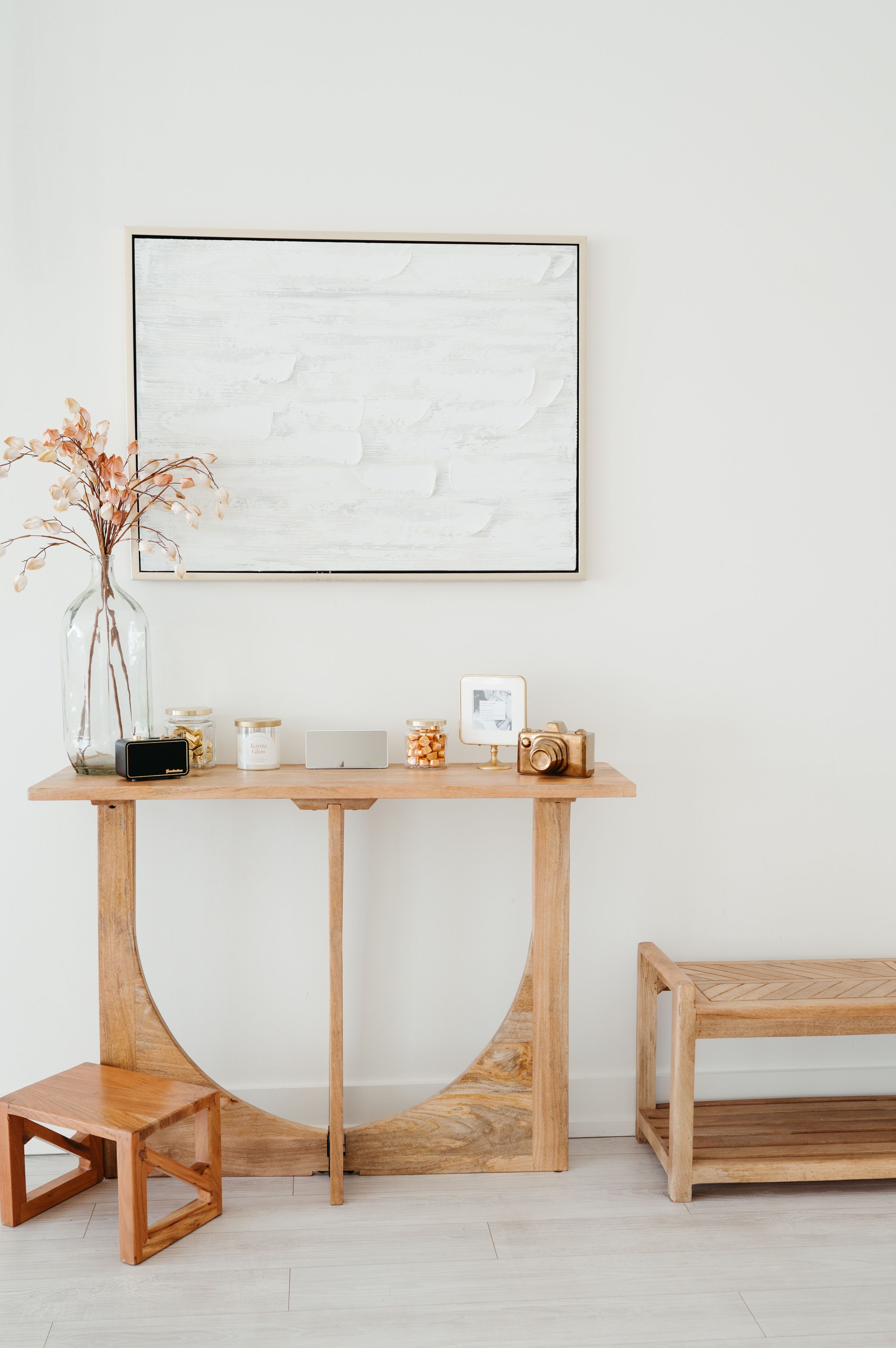 Minimalist entryway with wooden console table, framed art, and dried flowers in vase against white wall.