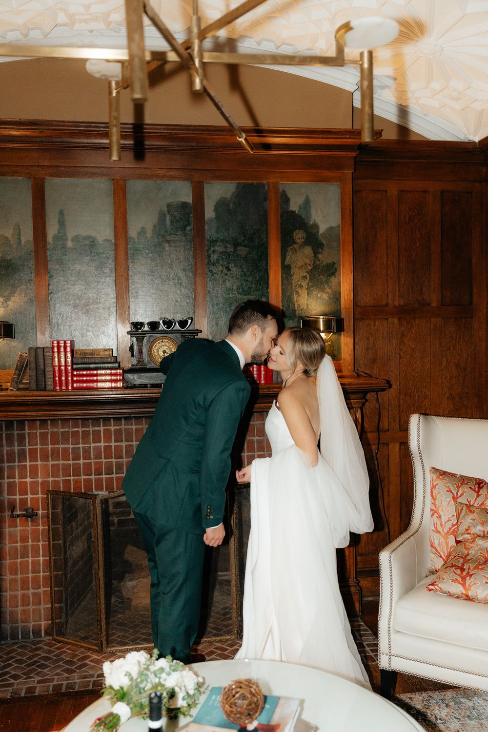 A romantic wedding moment by a vintage fireplace with antique decor and wood paneling.