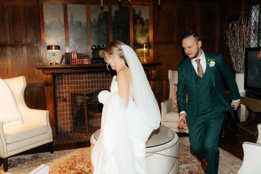 Couple in elegant wedding attire walking together in a rustic wooden room with vintage decor.