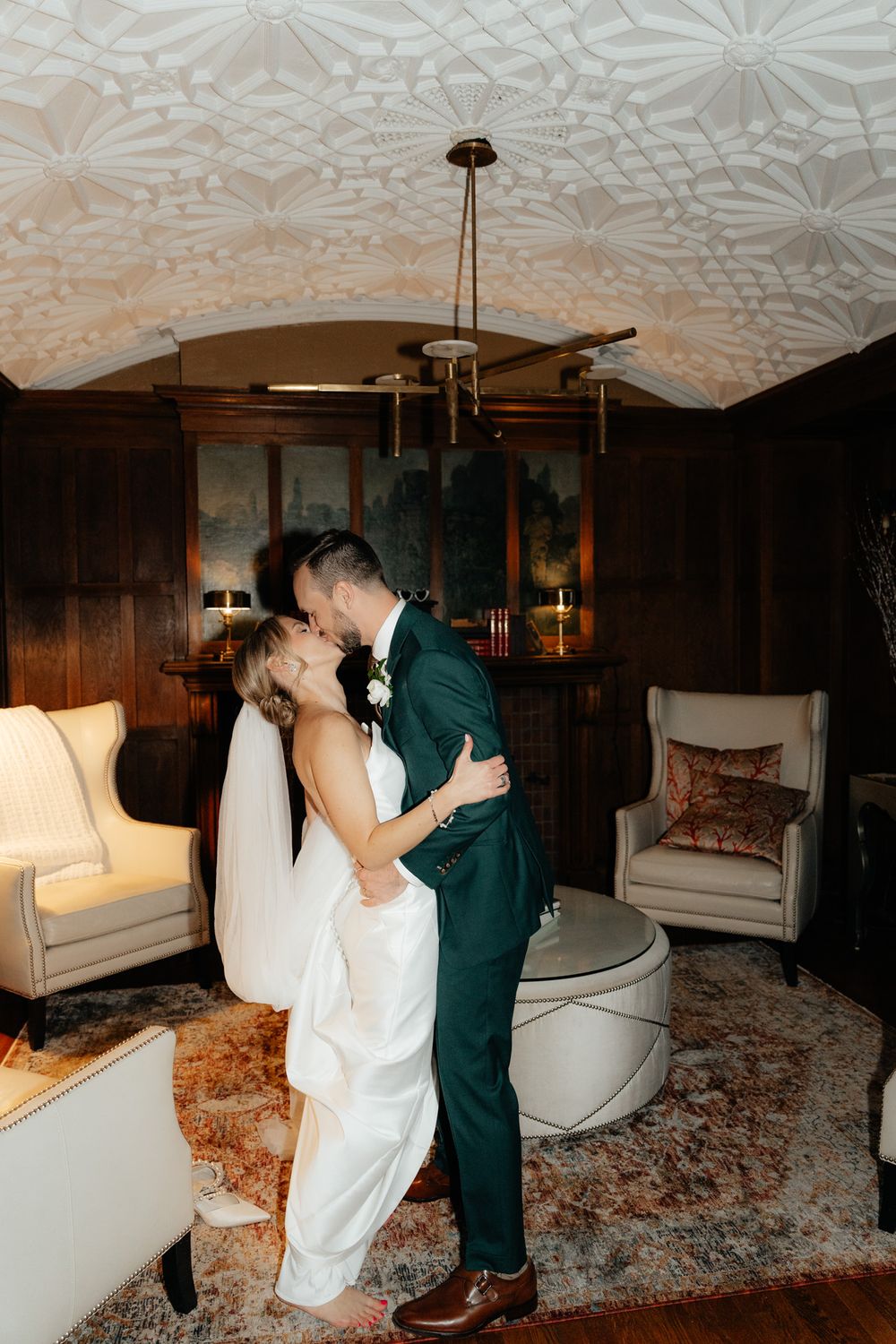 A couple shares an intimate moment in an elegant room with ornate ceiling details and vintage-style furniture.