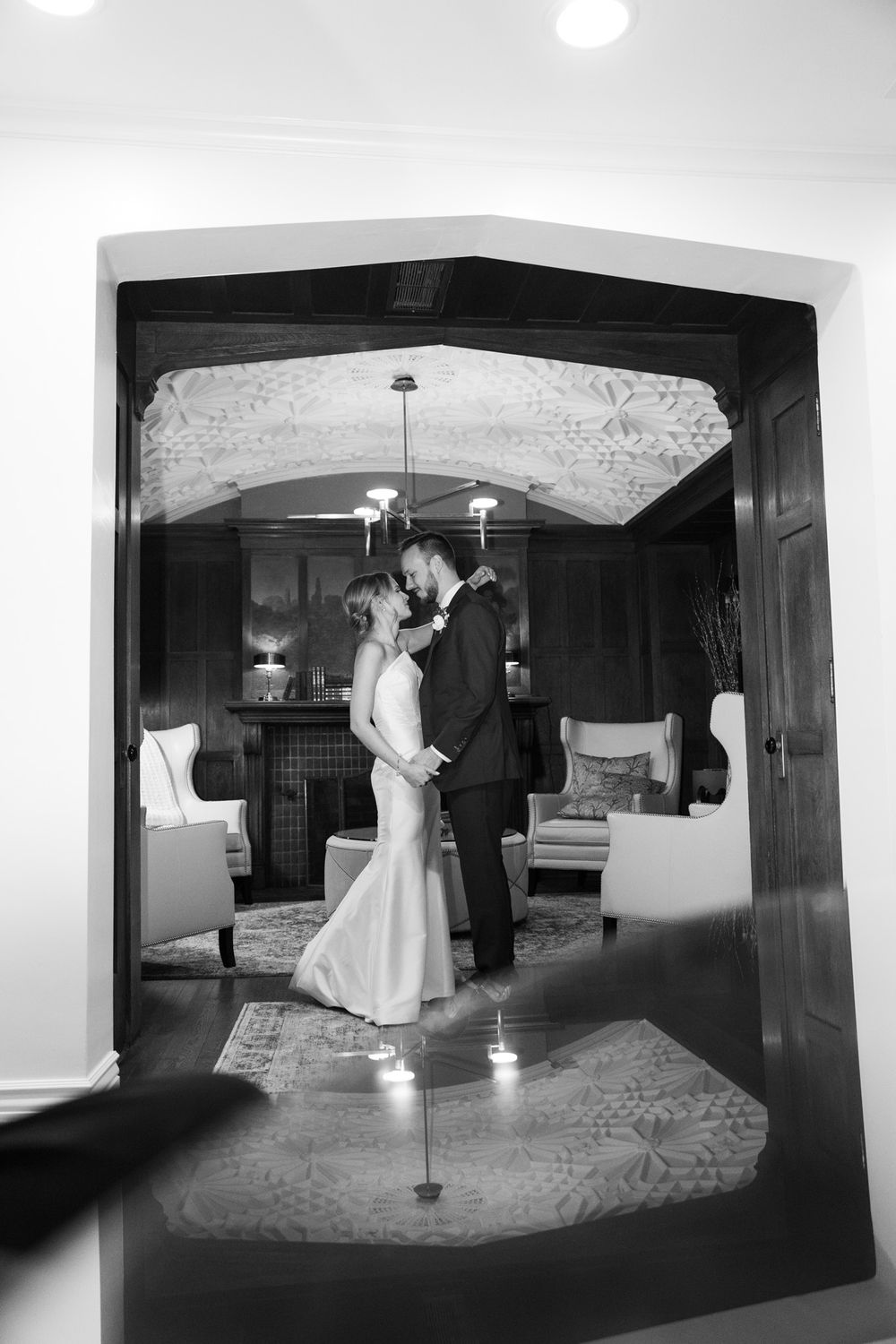 Black and white photograph of a couple sharing an intimate dance moment in an elegantly furnished room.