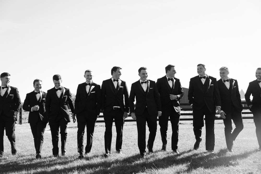 A historical black and white photograph showing a line of men in dark suits walking in unison across a field.