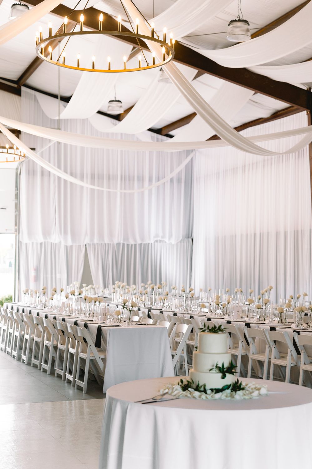 Elegant wedding reception venue with white draping, large circular chandeliers, and long banquet tables.