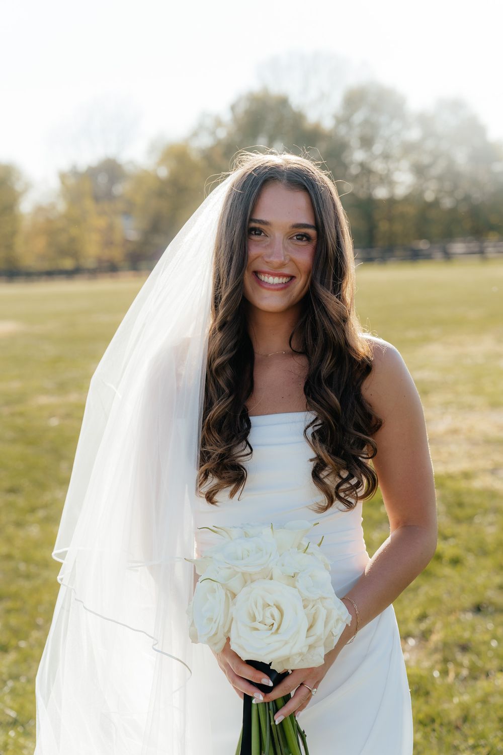 A wedding bouquet with white roses is held in a sunlit outdoor setting.