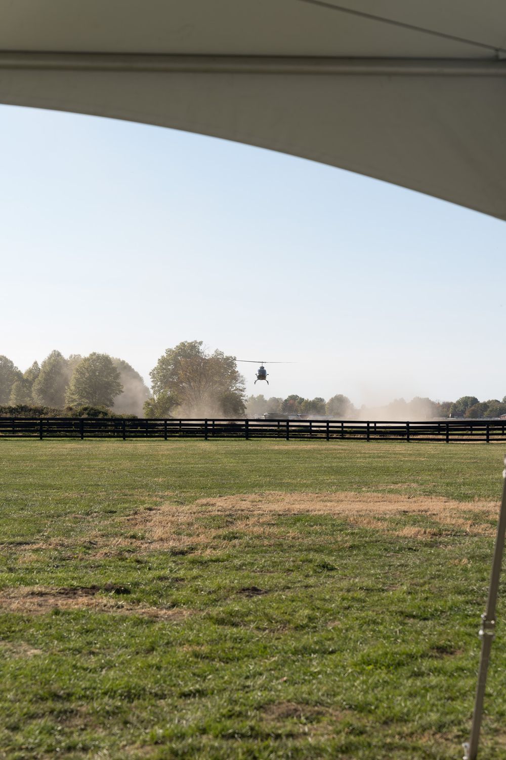 Morning mist hangs over a green pasture with wooden fencing and sprinkler system watering the field.