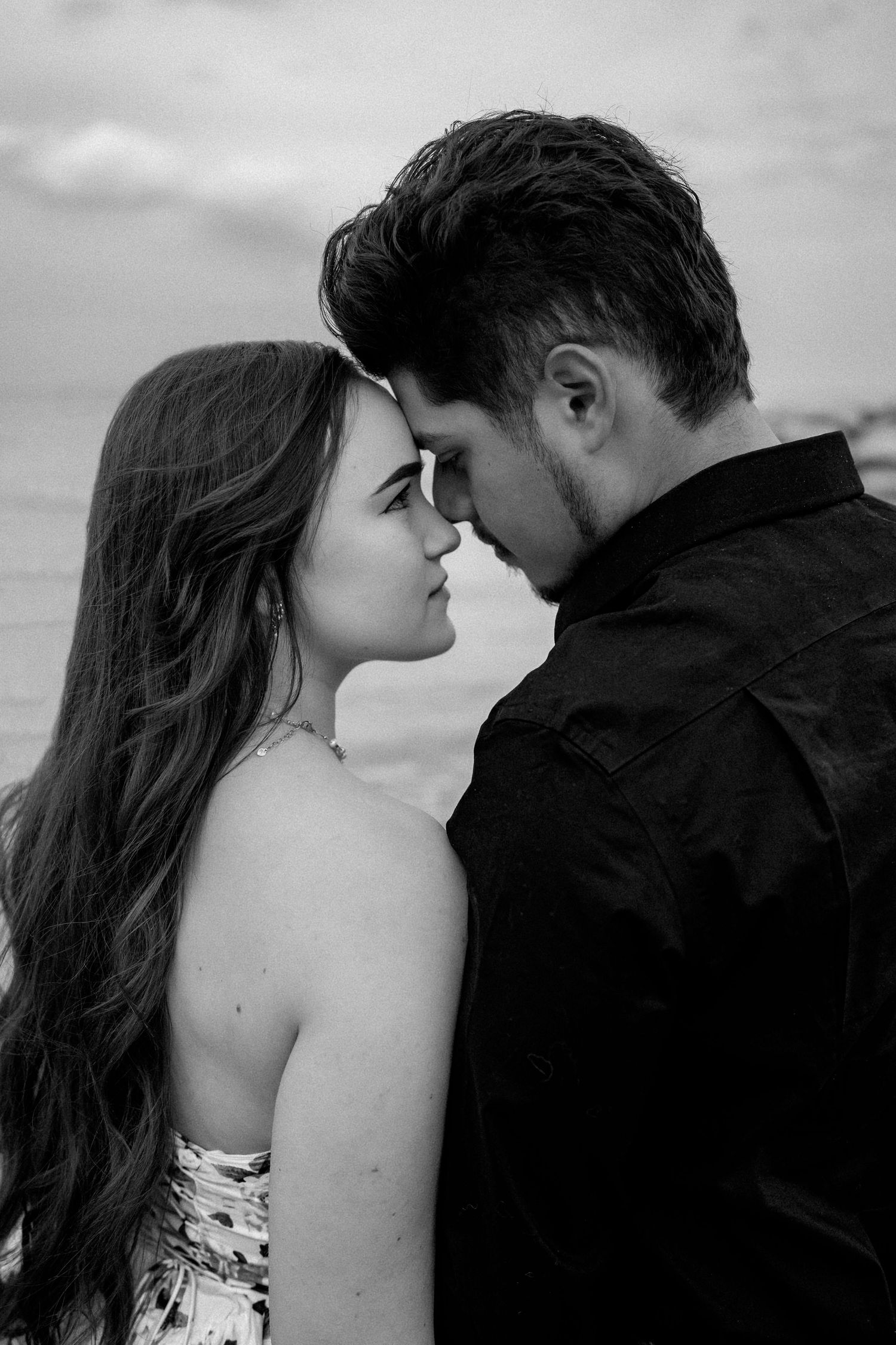 Romantic black and white portrait of couple in intimate moment against cloudy sky.