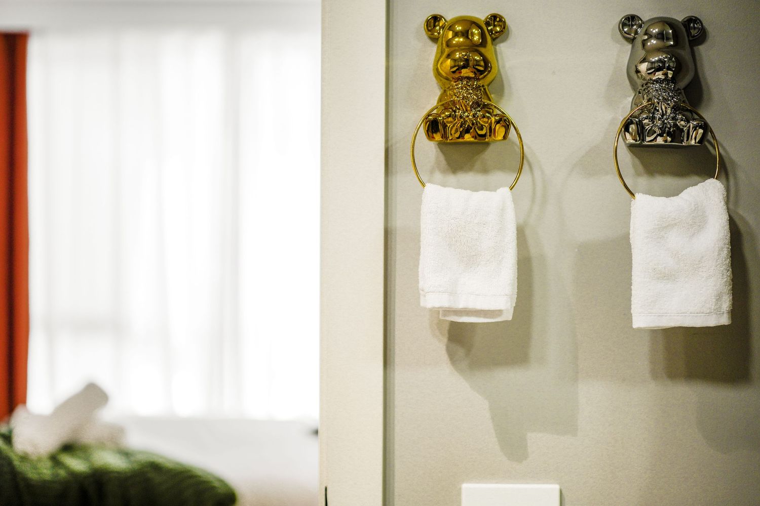 Two decorative bear-shaped toilet paper holders mounted on a wall, one gold and one silver colored.