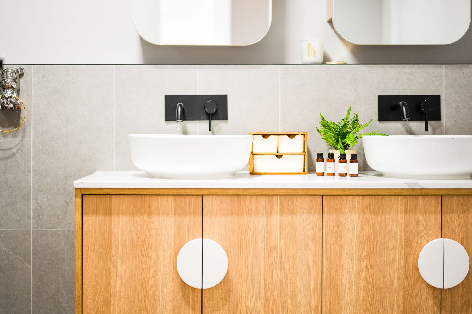 Modern bathroom vanity with light wood cabinets, dual sinks, white countertop, and decorative plant display.