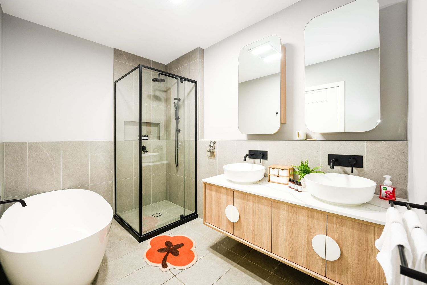 Modern bathroom interior with freestanding tub, glass shower enclosure, and floating wood vanity with double vessel sinks.