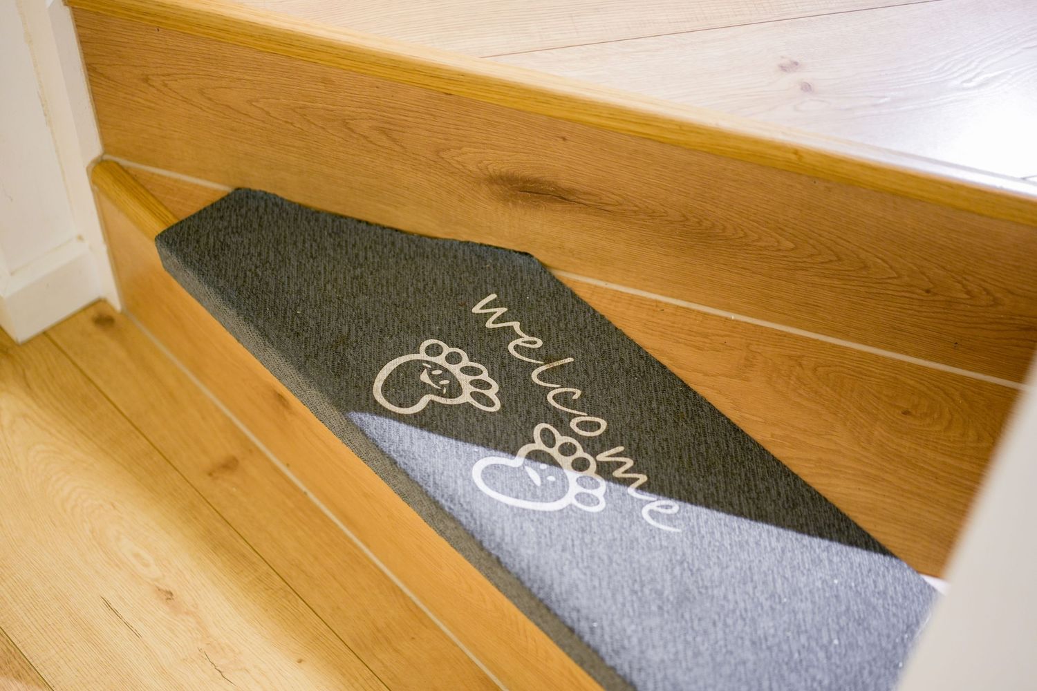 Diagonal grey and black pattern doormat or floor mat with bicycle design resting on wooden floorboards.
