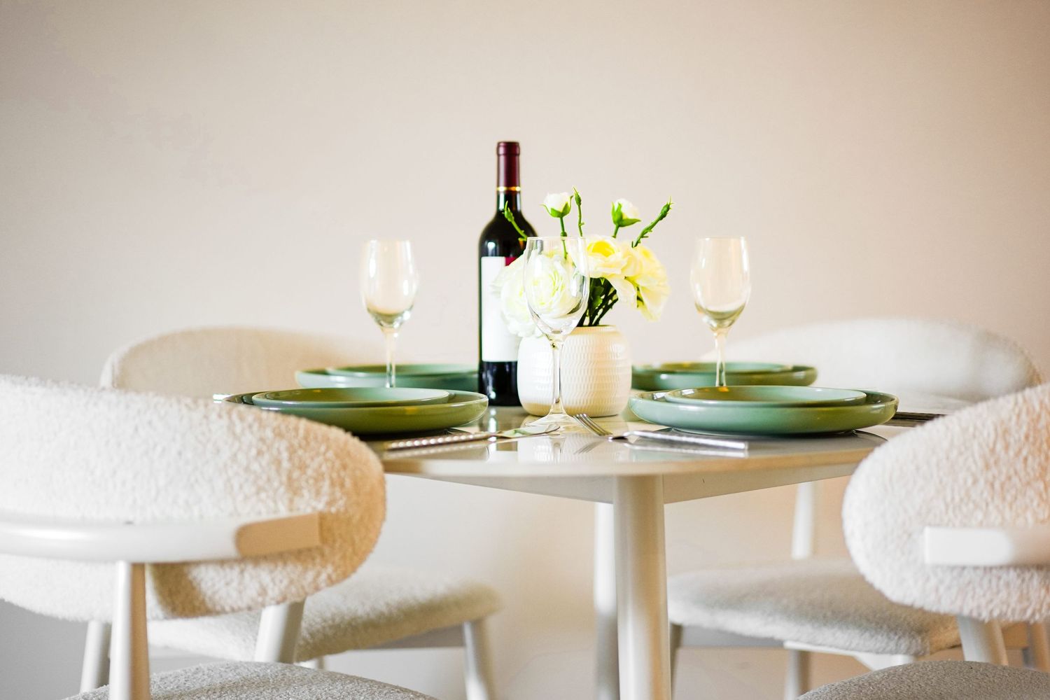 Intimate table setting with wine bottle, green plates, and white floral centerpiece on round white dining table.