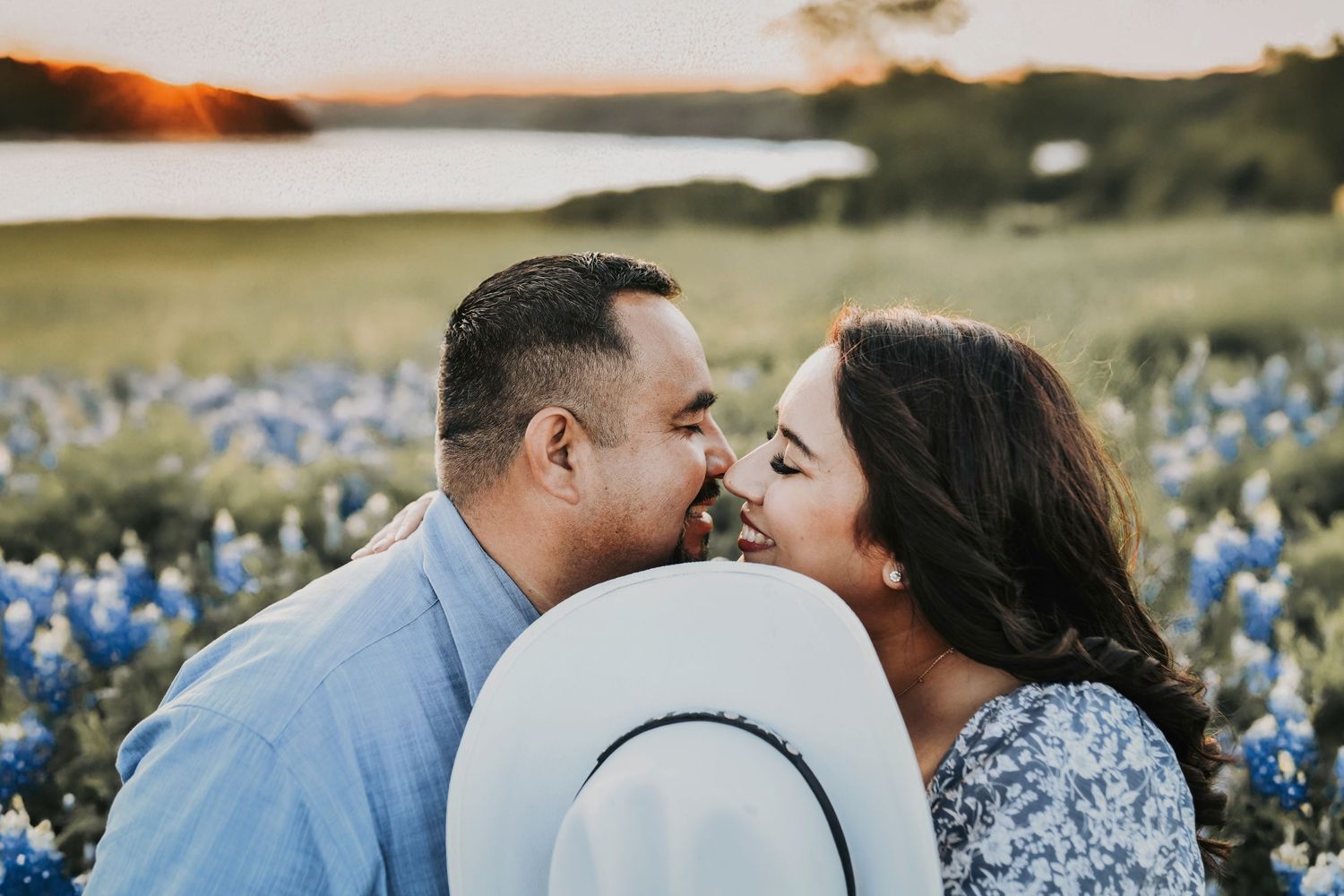 Groom-to-be lifting fiancée off her feet among vibrant bluebonnets with the lake in the background