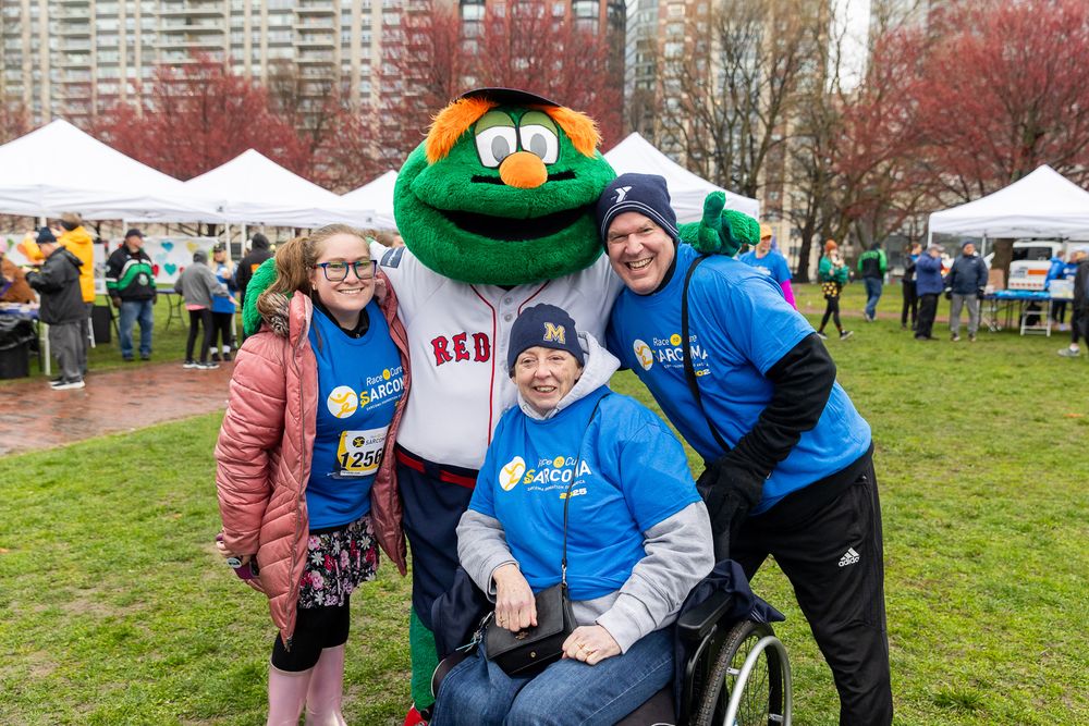 Wally the Green Monster mascot poses with supporters at an outdoor charity event on a fall day.