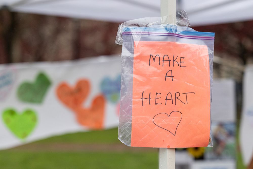 A pink sticky note with 'Make a Heart' written on it hangs alongside colorful heart shapes in the background.