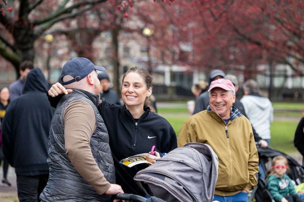 A group of people gathered outdoors on a cold day for a casual conversation in a park with red autumn foliage.