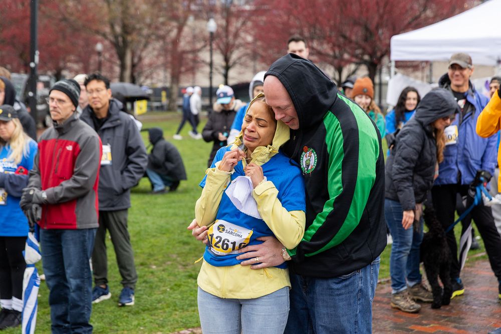 Marathon spectators gather in chilly weather to support runners during a rainy race day in Boston.