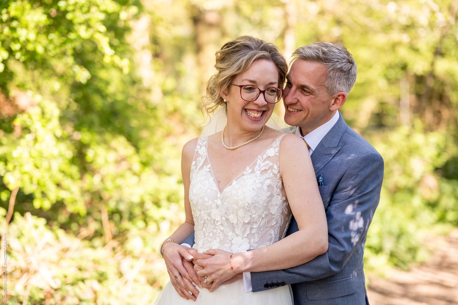 Joyful couple embraces in outdoor garden setting with soft natural lighting filtering through trees.