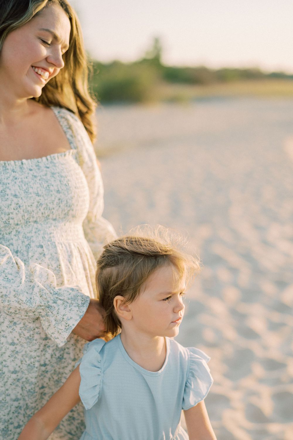 A sun-drenched beach scene capturing a tender moment between someone in white and a child in blue.