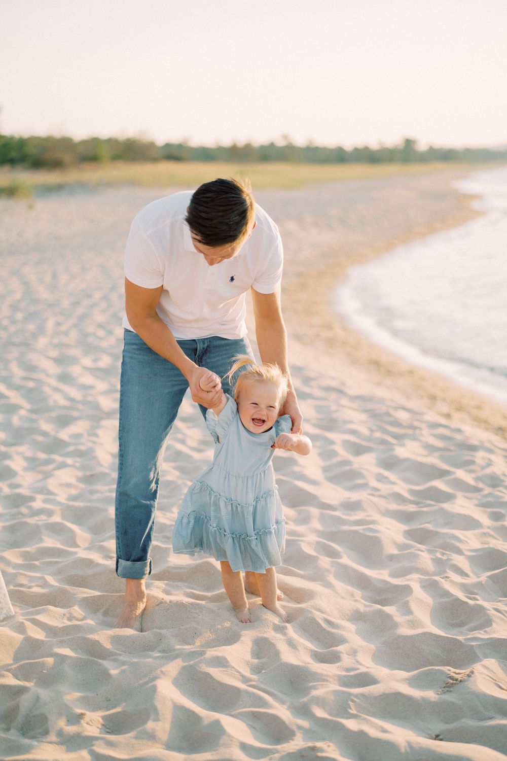 A playful moment on the beach between someone and a small child in a blue dress.