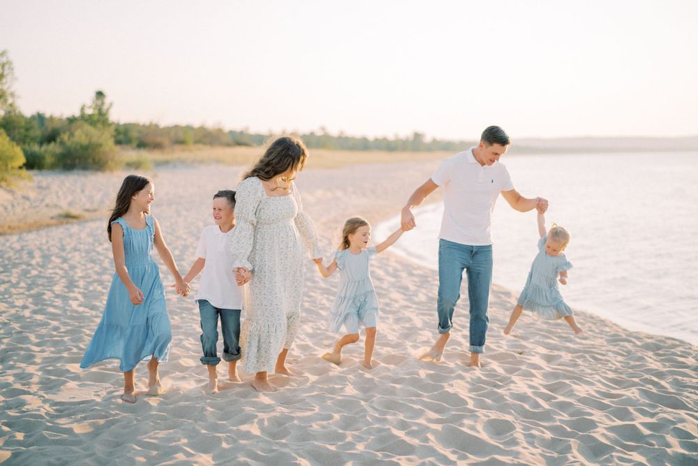 A family walking hand-in-hand along a scenic beach at sunset in coordinated outfits.