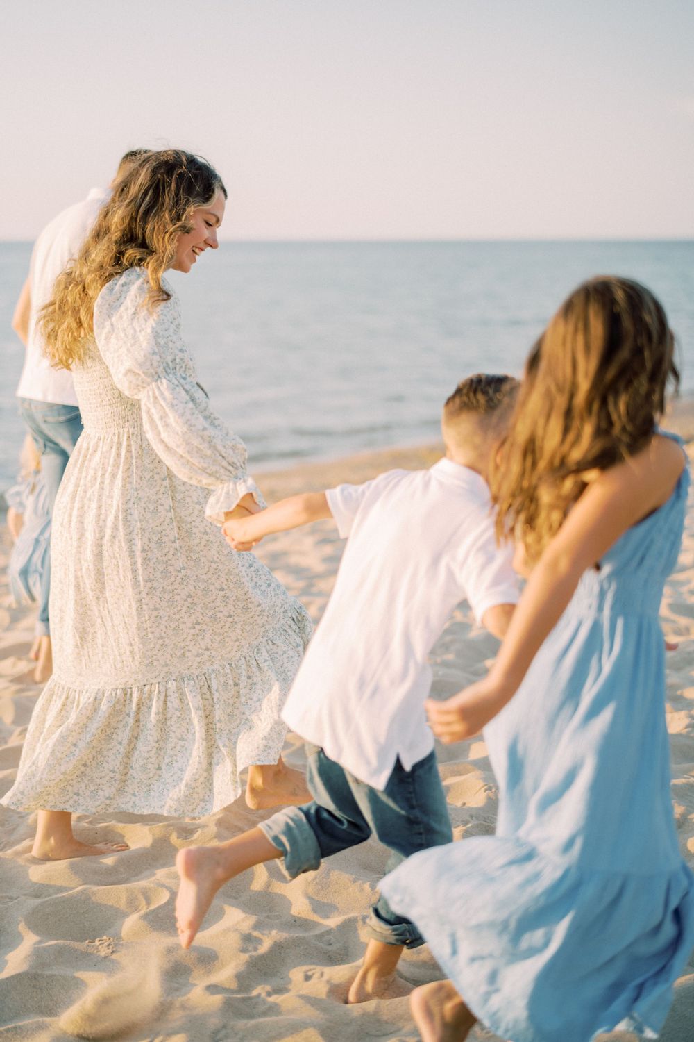 Family playing and dancing together on a sandy beach at sunset with light flowing dresses.