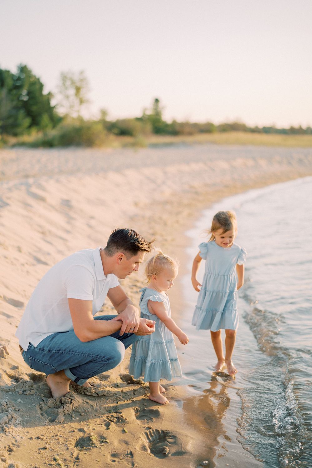 Family exploring the water's edge together on a peaceful beach during sunset.