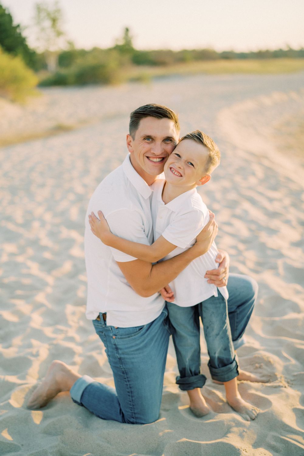 Joyful embrace between parent and child kneeling on sandy beach.