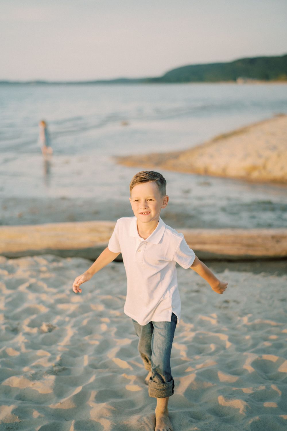 Child running and playing on beach sand during golden hour with ocean in background.