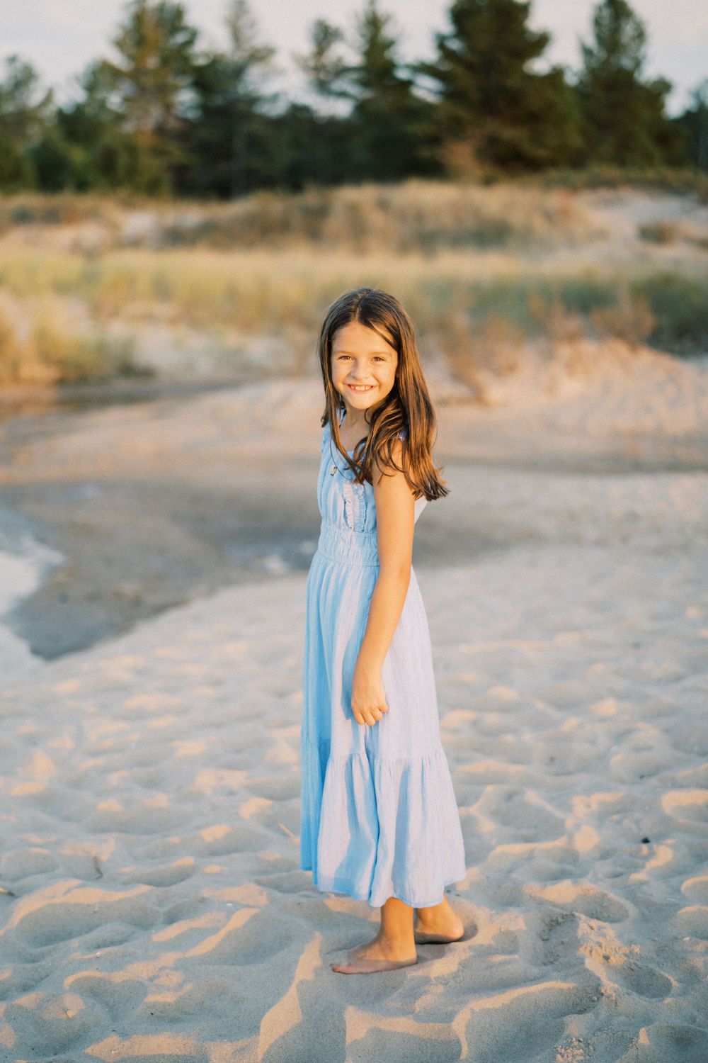 A light blue summer dress catches the golden light as someone poses on a sandy beach at sunset.