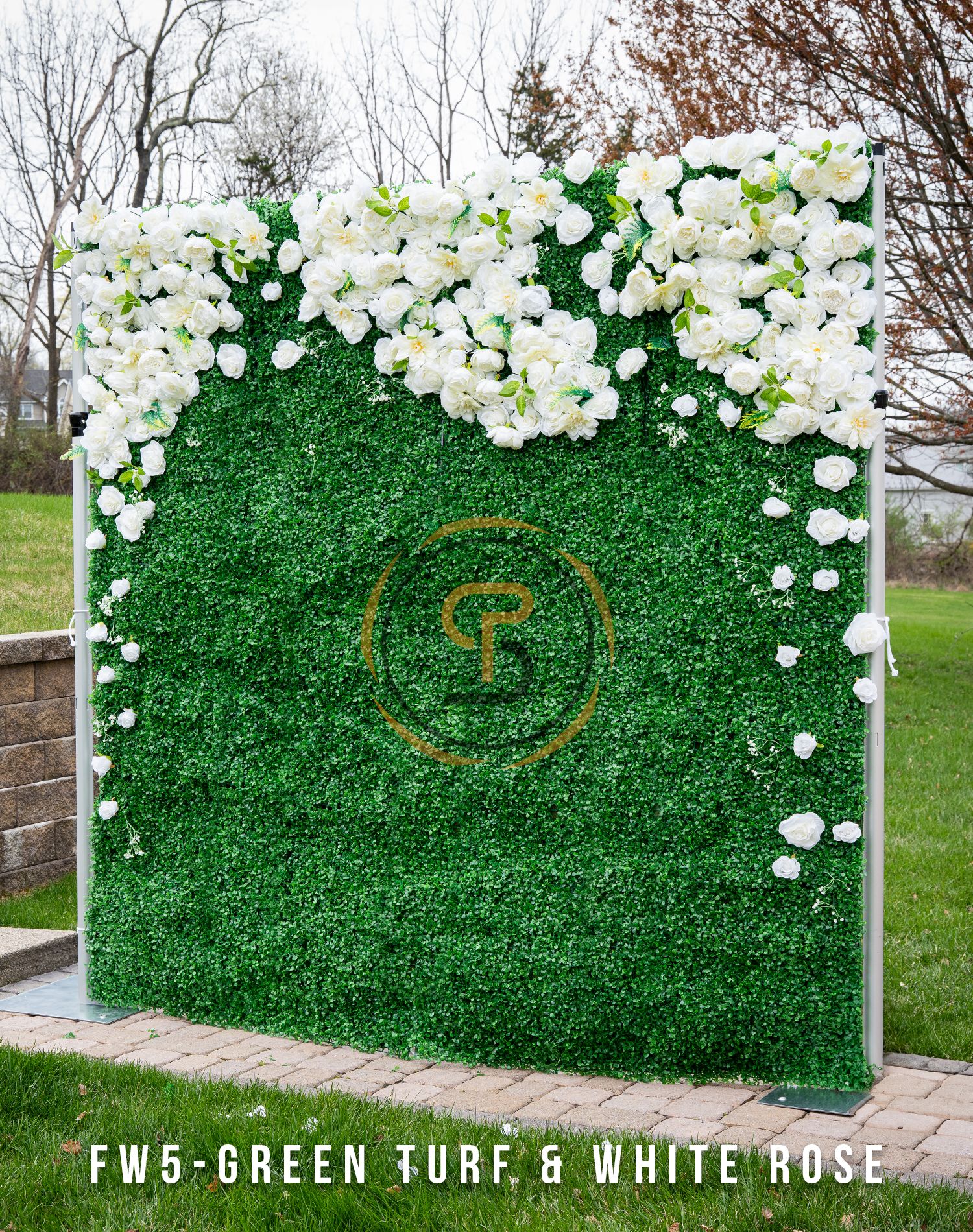 Green turf wall with cascading white roses and golden circular logo design.