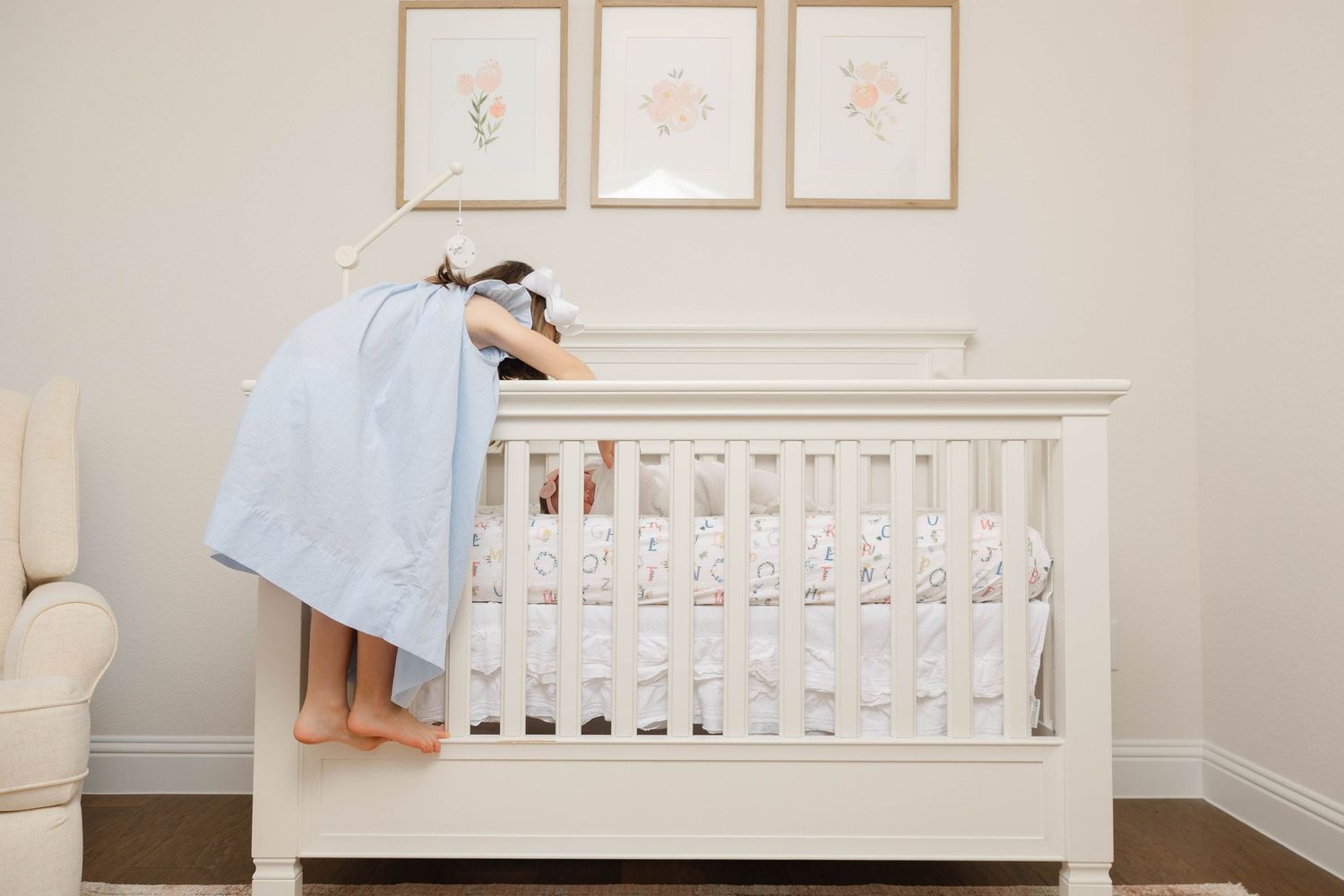 Person in blue dress leans over white baby crib in minimalist nursery with framed wall art.