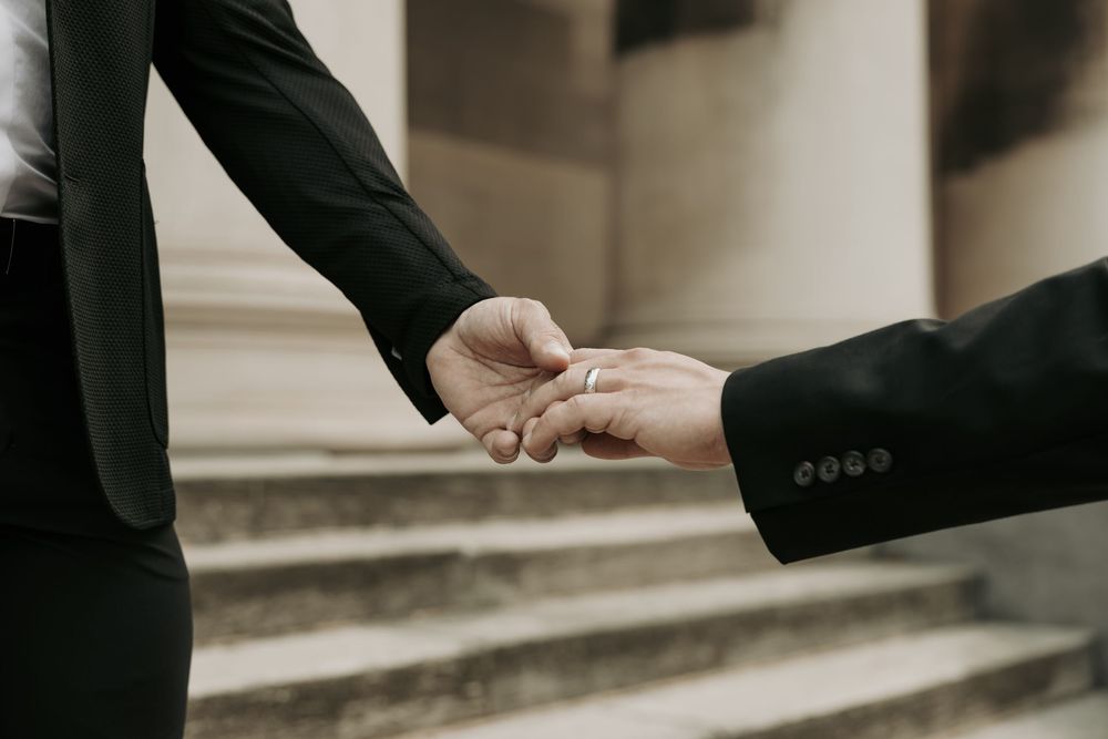 Two people in business attire exchanging a handshake on stone steps, photographed in muted tones.