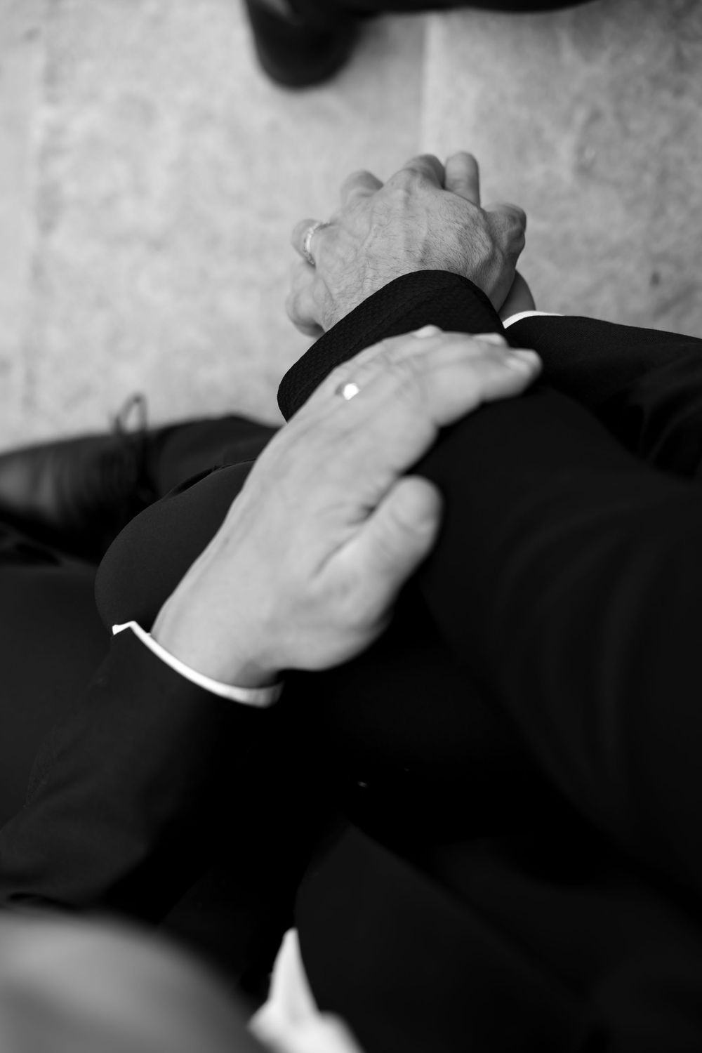 Hands clasped in prayer or contemplation on dark fabric, captured in black and white photography.