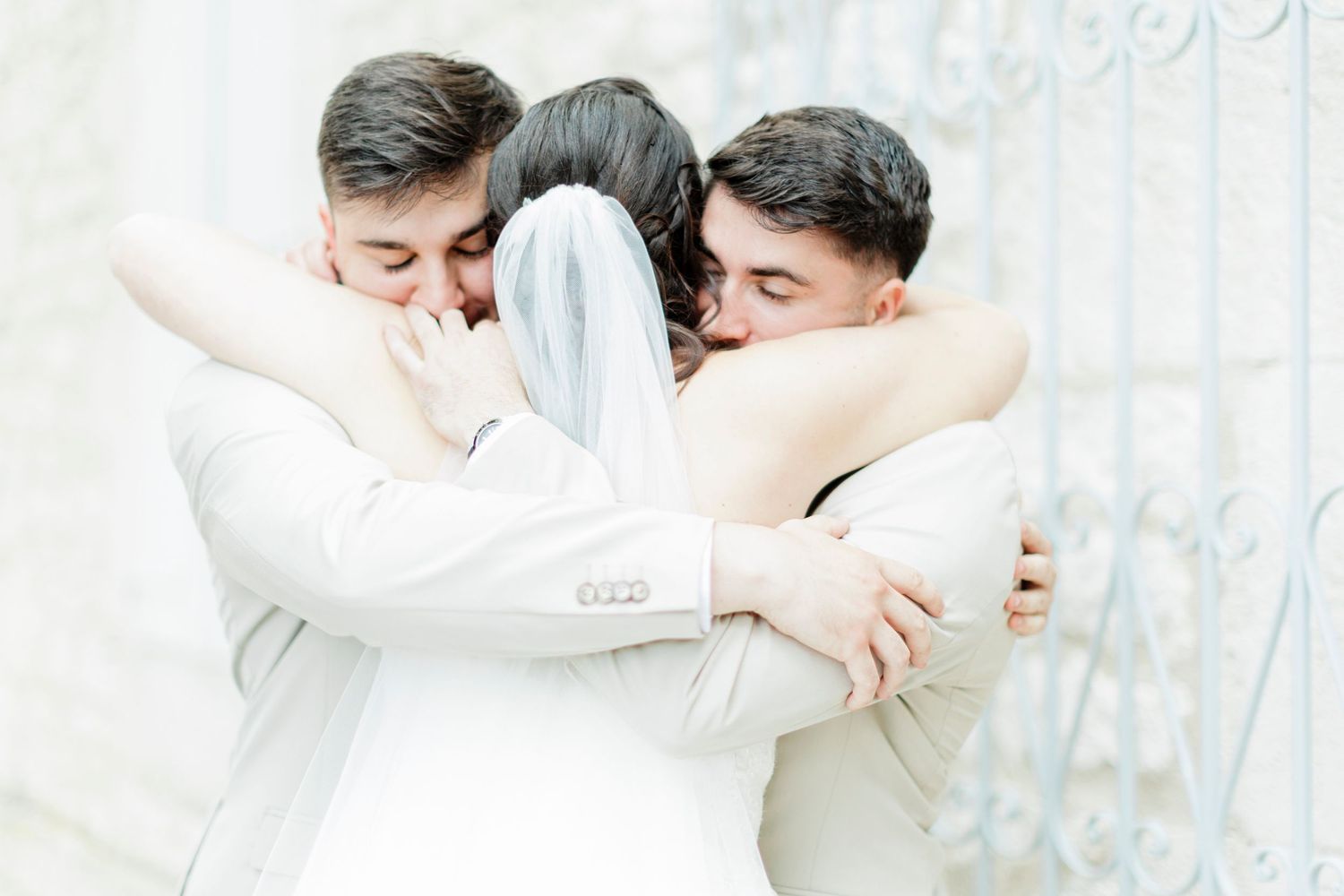 Three people share an emotional group hug in white formal attire.