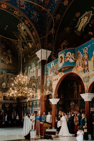 Religious ceremony inside an ornate orthodox church with vaulted ceilings, vibrant frescoes, and crystal chandelier.