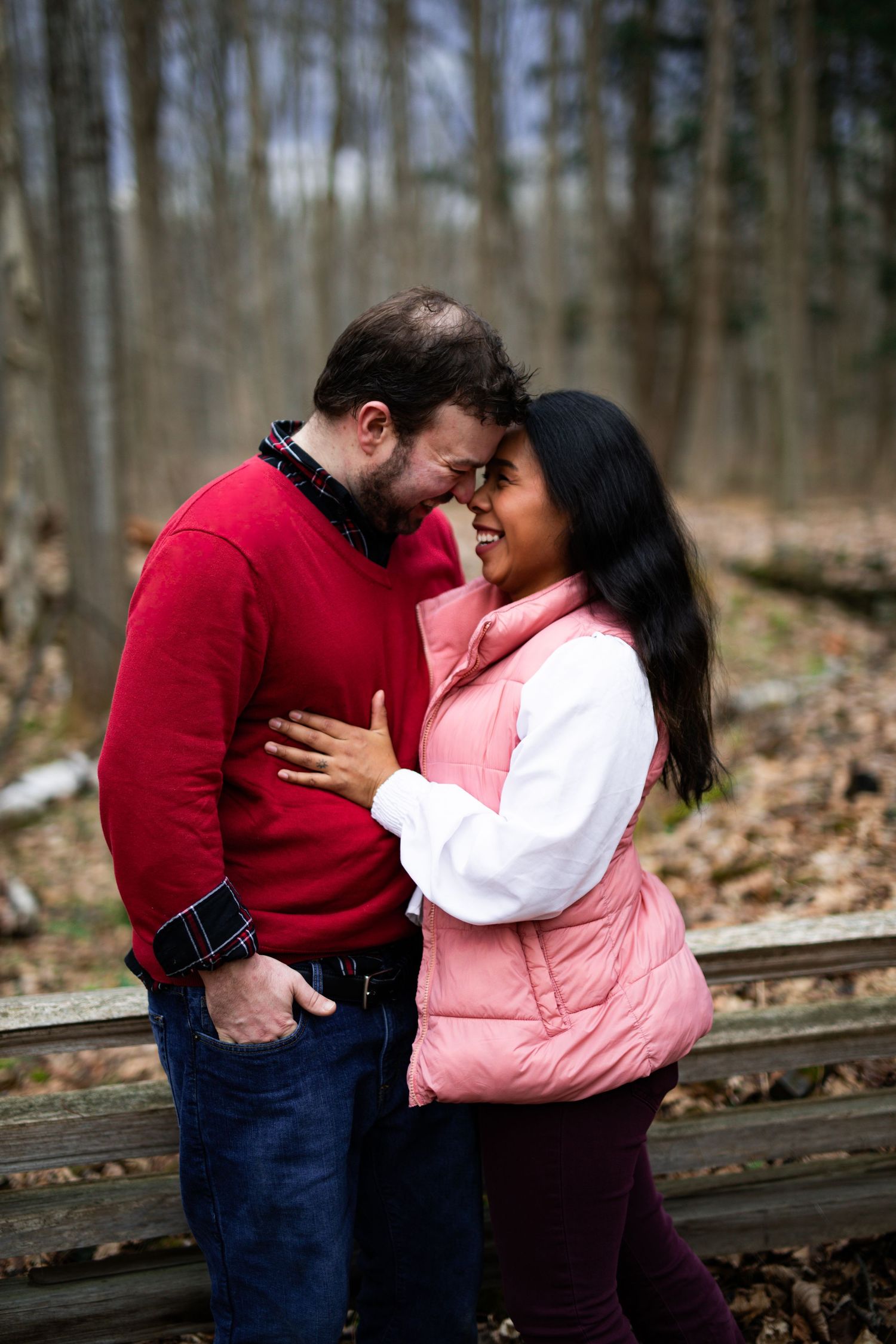 A couple shares an intimate moment together outdoors while standing on wooden steps in a forest setting.