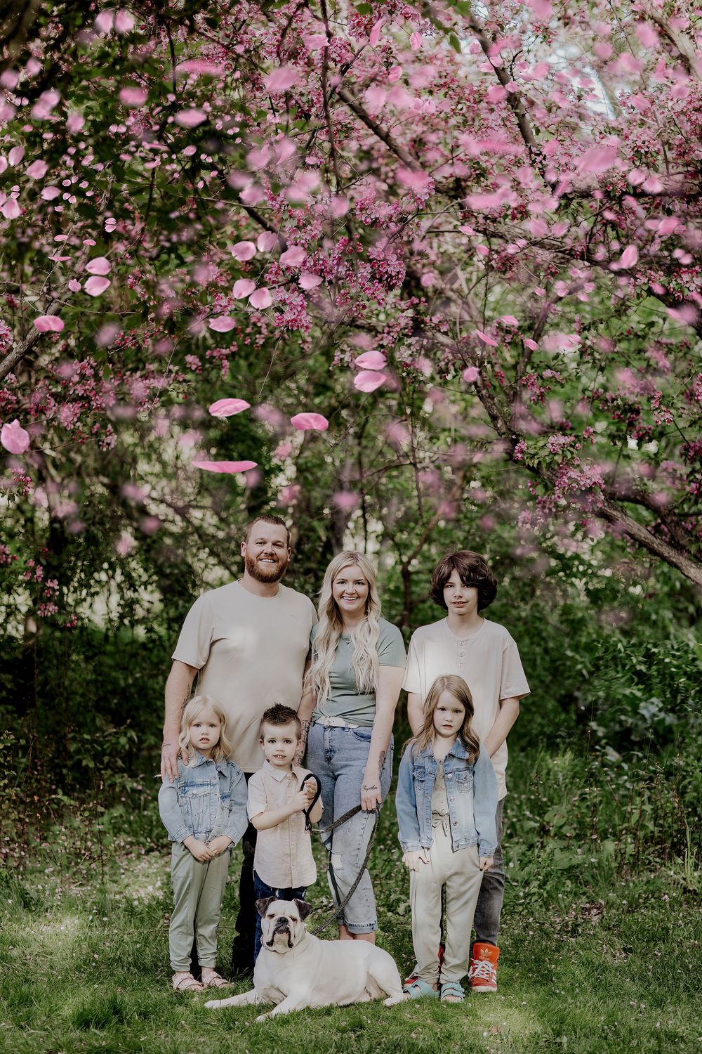 A group poses together under blooming pink cherry blossoms on a spring day with their white dog.