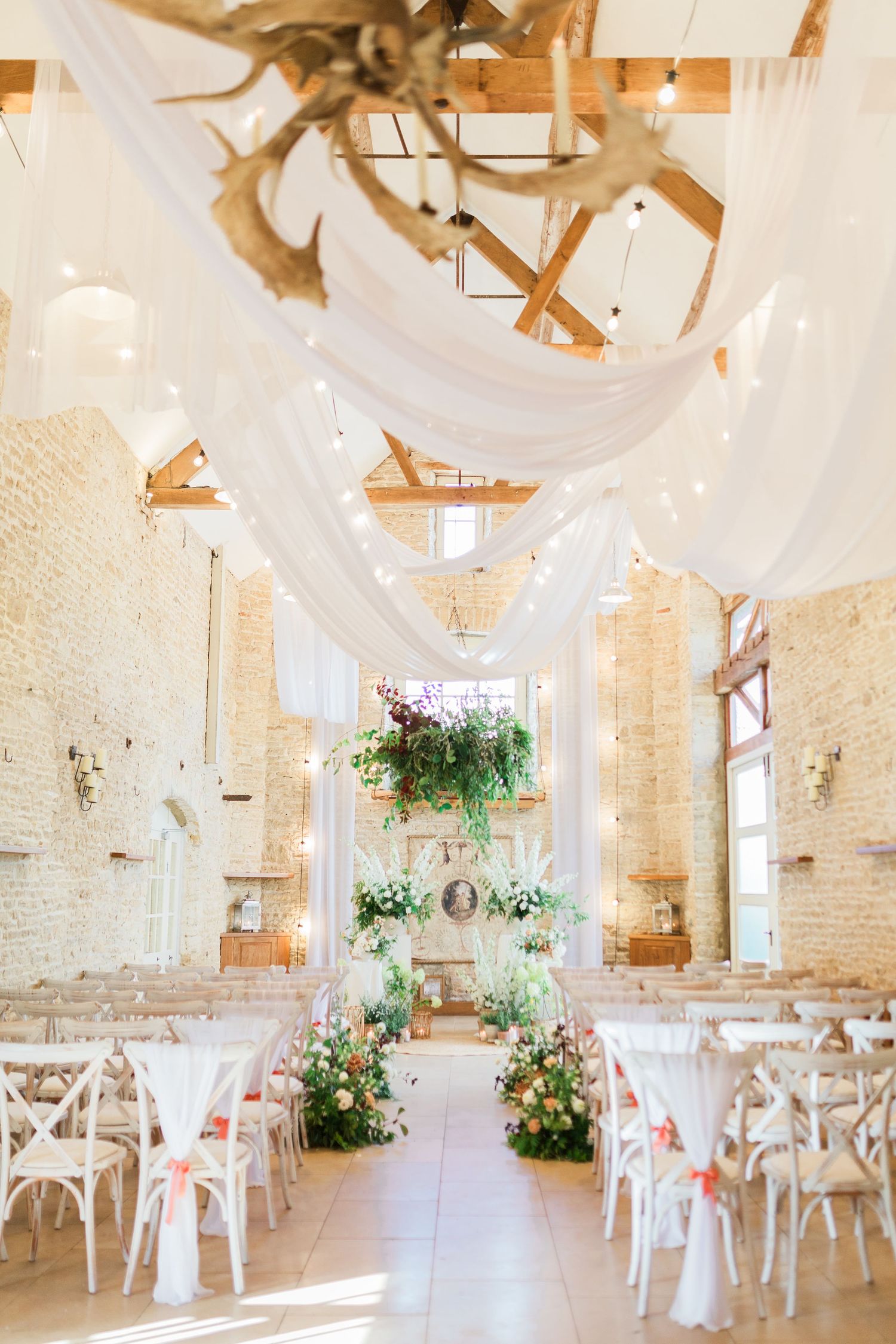 Elegant indoor wedding with white draping, floral arrangements, and white chairs at Merriscourt Oxfordshire by Hayley Elizabeth Photography