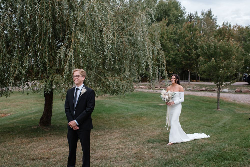 A couple shares their first look moment under a weeping willow tree at an outdoor wedding venue.