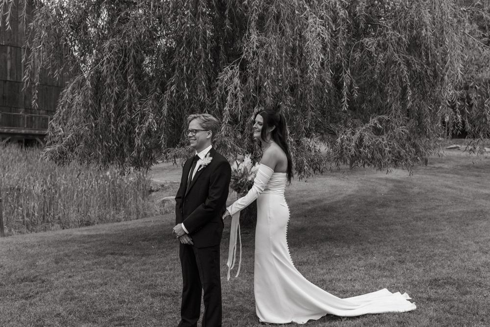 Black and white wedding photo showing a couple standing under a willow tree during their first look moment.