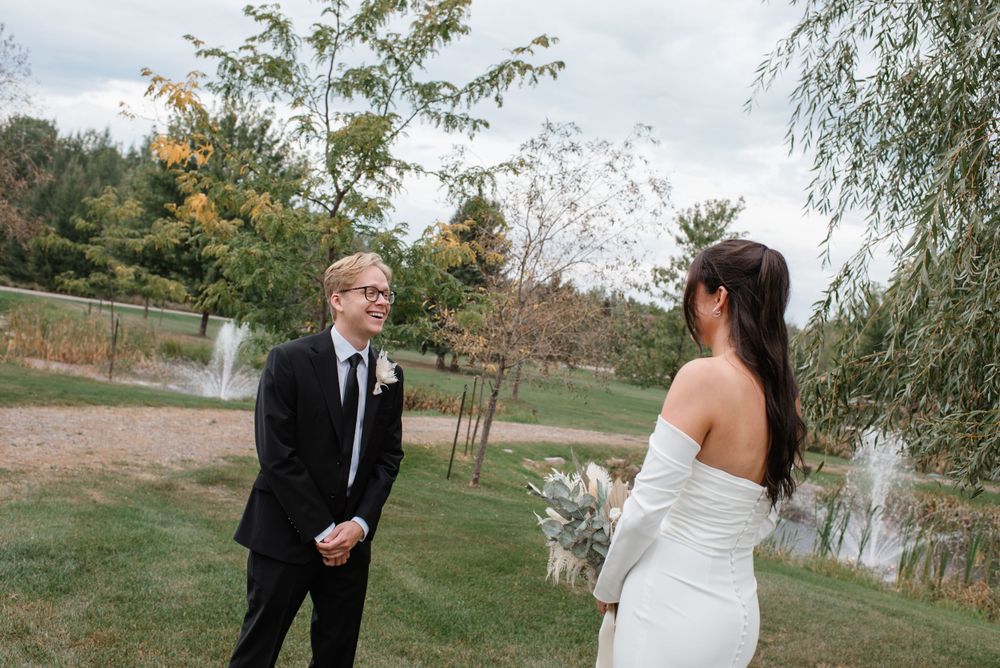 A couple shares an intimate first look moment in their formal wedding attire on a grassy lawn.