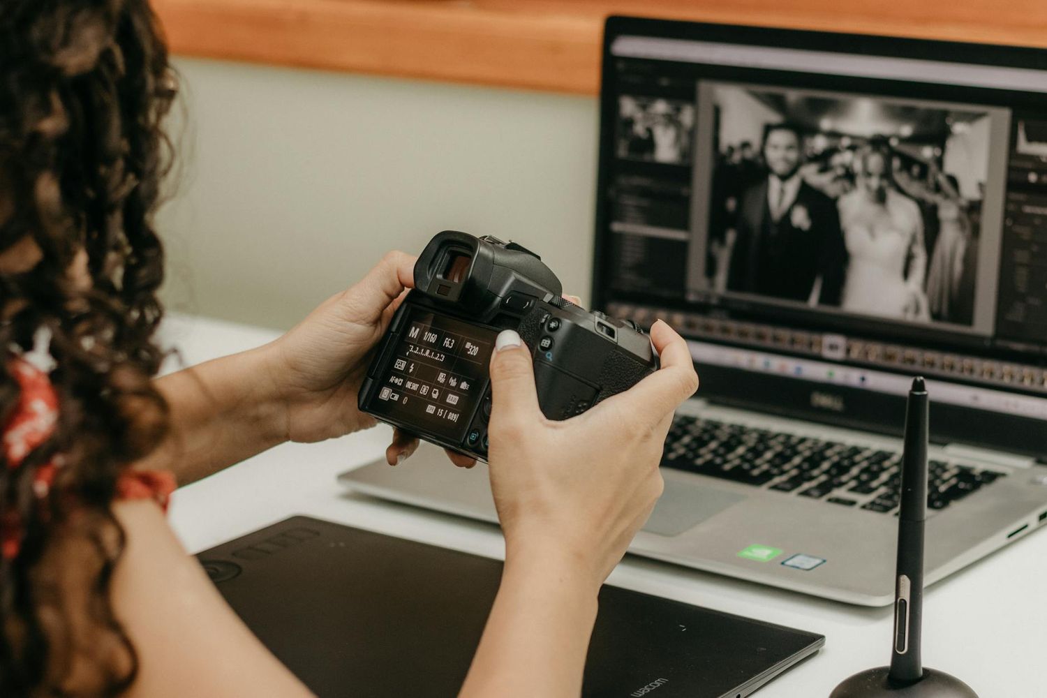 Photographer reviewing wedding images on camera display while editing photos on laptop computer.