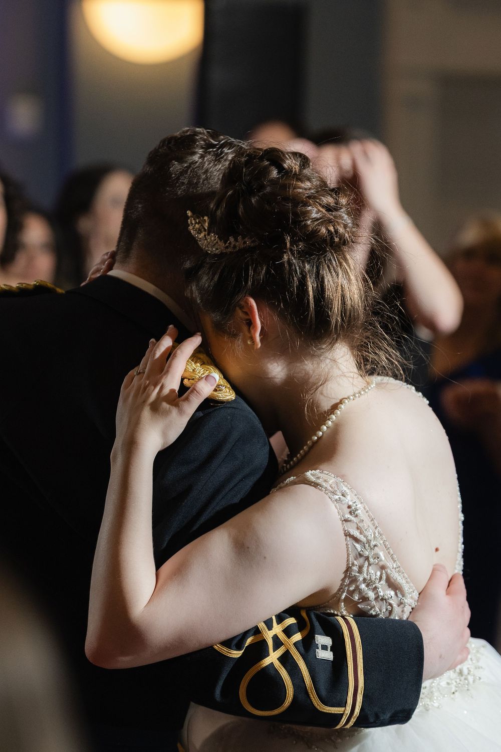 Romantic couple embraces during first dance at wedding reception with bride in white lace dress and glistening lights.