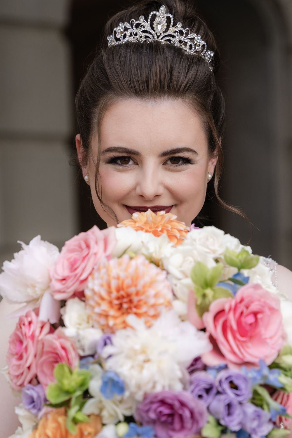 Colorful bridal bouquet with pink roses, orange dahlias, and purple flowers paired with a silver tiara.