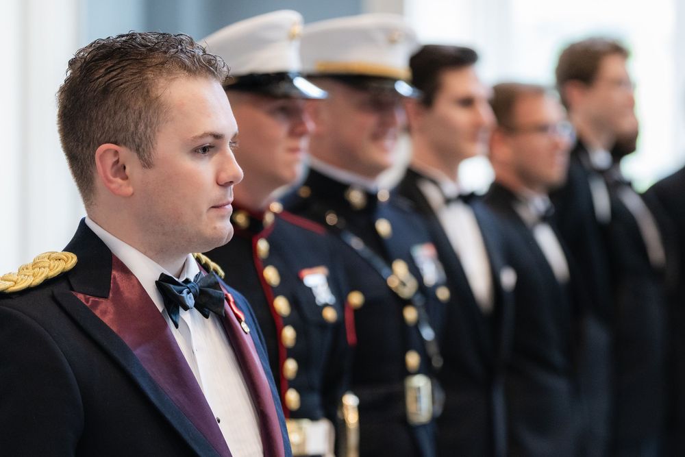 Several people in formal dress and military uniforms stand in a line during what appears to be a ceremonial event.